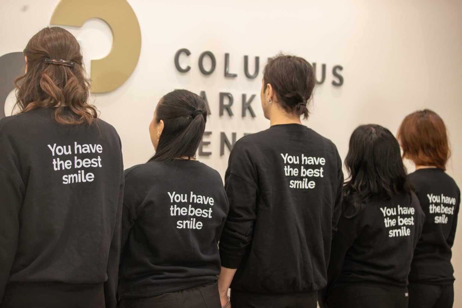 The Columbus Park Dental team wearing “You have the best smile” jackets in front of the practice sign